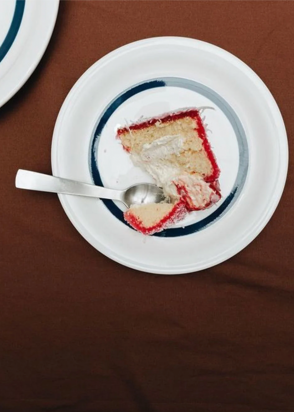 Slice of cake on a plate with a spoon, on a brown surface