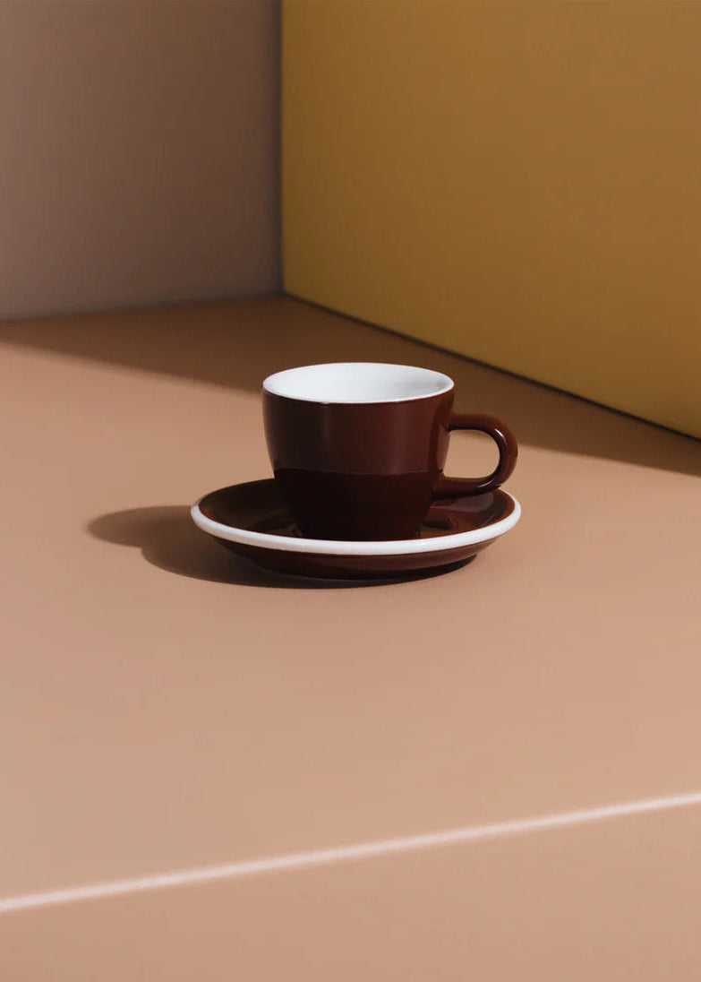 Brown coffee cup and saucer on a beige surface with a yellow wall in the background