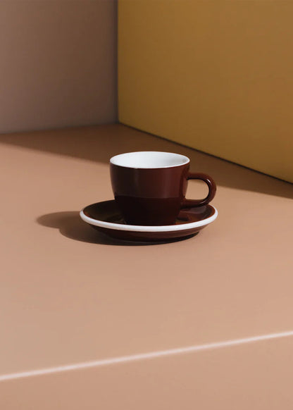 Brown coffee cup and saucer on a beige surface with a yellow wall in the background