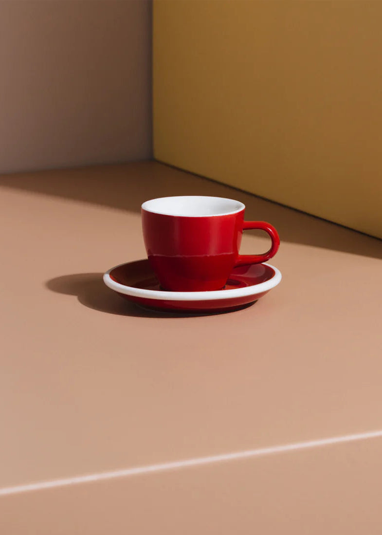 Red coffee cup and saucer on a beige surface with a brown wall background