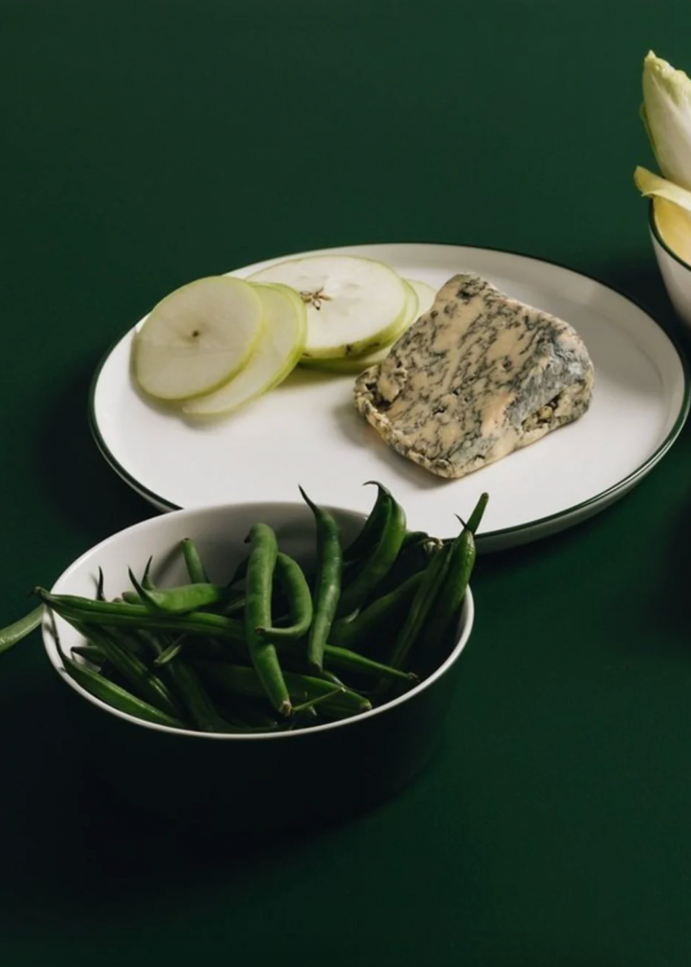 Platter with blue cheese, sliced pears, and green beans on a dark green background