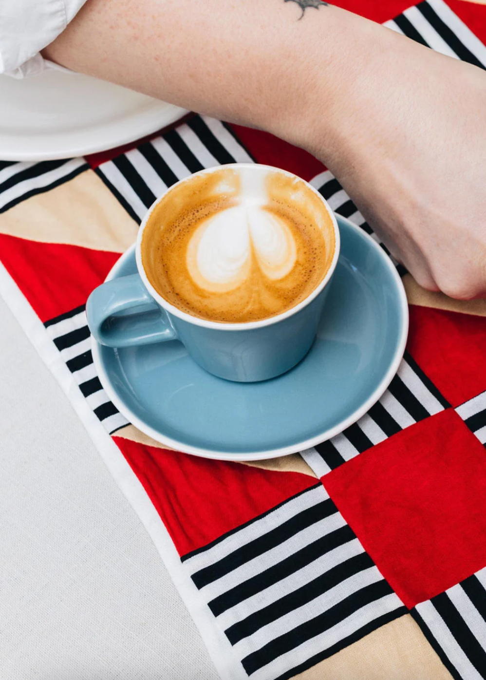 Cappuccino in a blue cup on a saucer with a geometric-patterned tablecloth