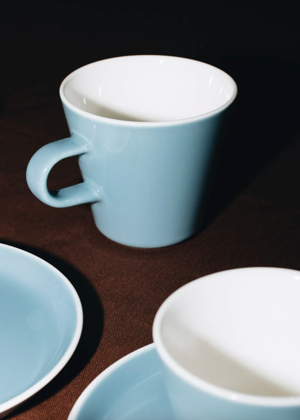 Set of blue ceramic mugs and saucers on a dark surface