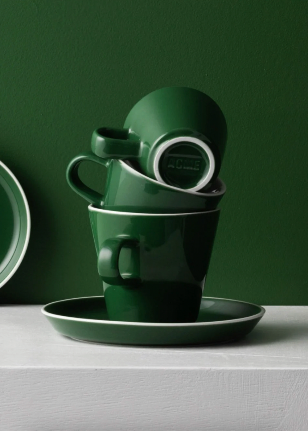 Green ceramic cups and saucers on a white surface with a dark green background