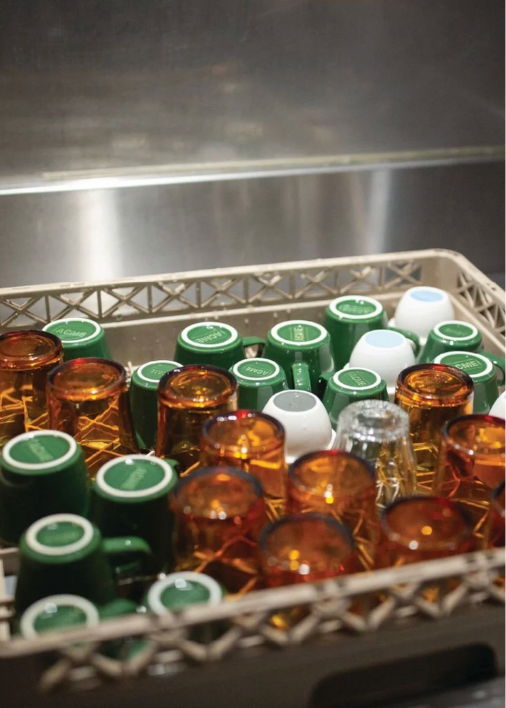 Assorted glass and ceramic mugs in a plastic dishwasher tray with a metallic background