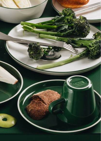 Green ceramic cup and saucer on a green table with bread and broccoli