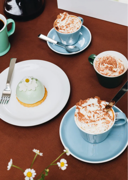 Café setting with blue coffee cups and saucers, a pastry on a plate, and a small cake on a brown table.
