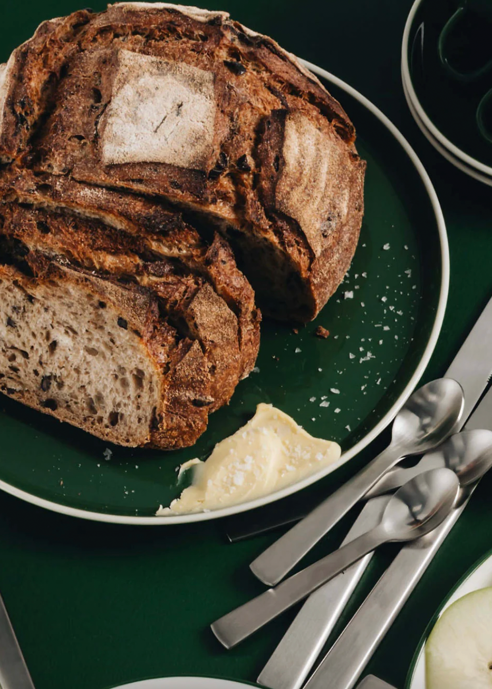 Loaf of bread on a green plate with silver cutlery on a dark surface