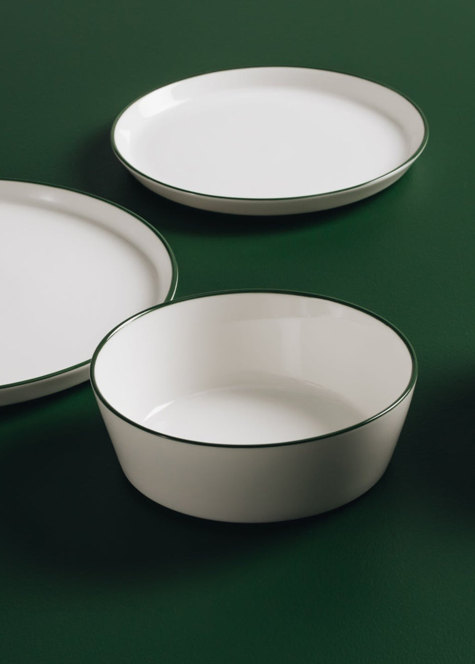 Set of white ceramic plates with green rims on a dark green background