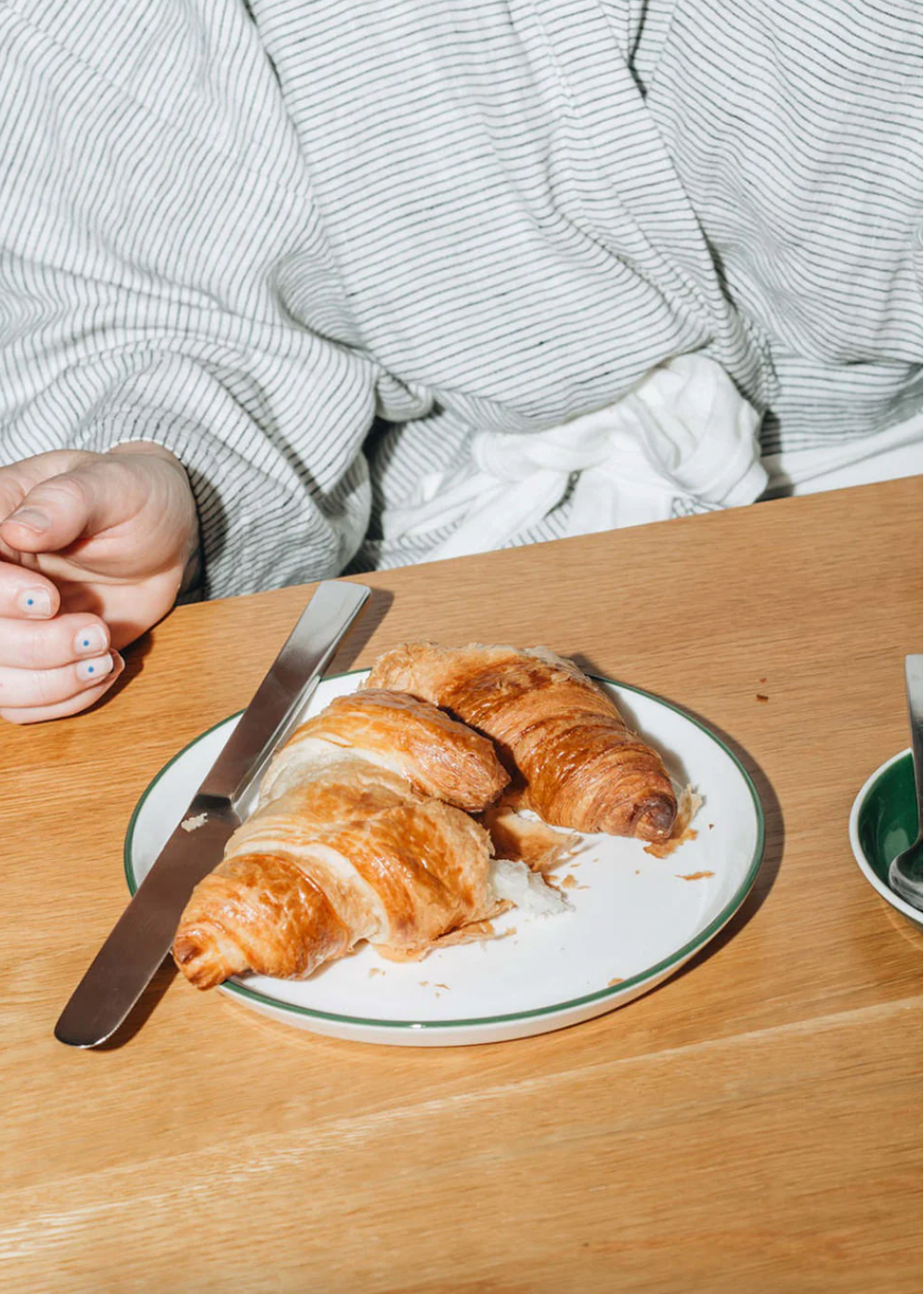 Person sitting at a table with a plate of croissants and a knife on a wooden surface.