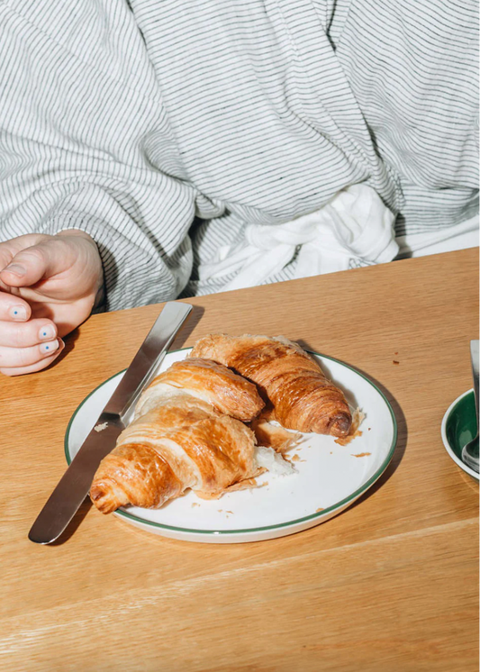 Person sitting at a table with a plate of croissants and a knife on a wooden surface.