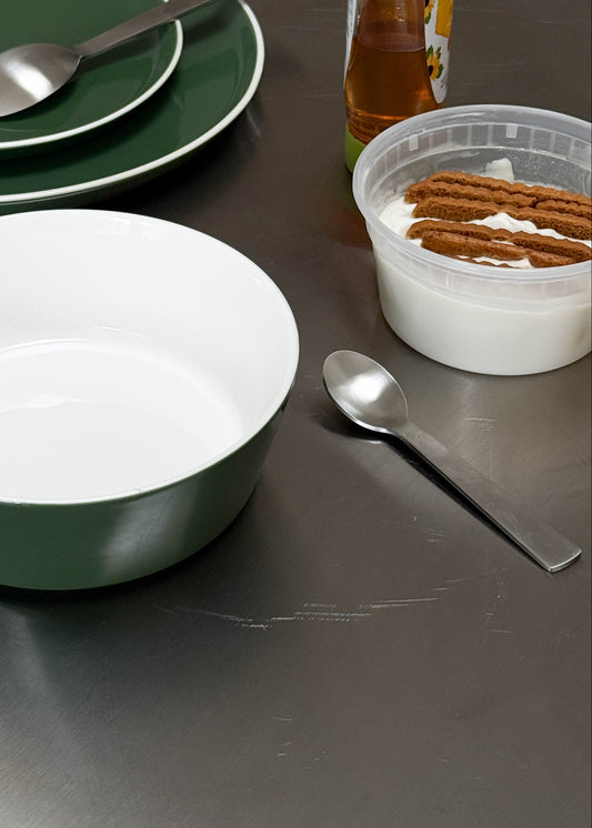 Green ceramic bowls and a white bowl on a metallic surface with utensils and a container of snacks.