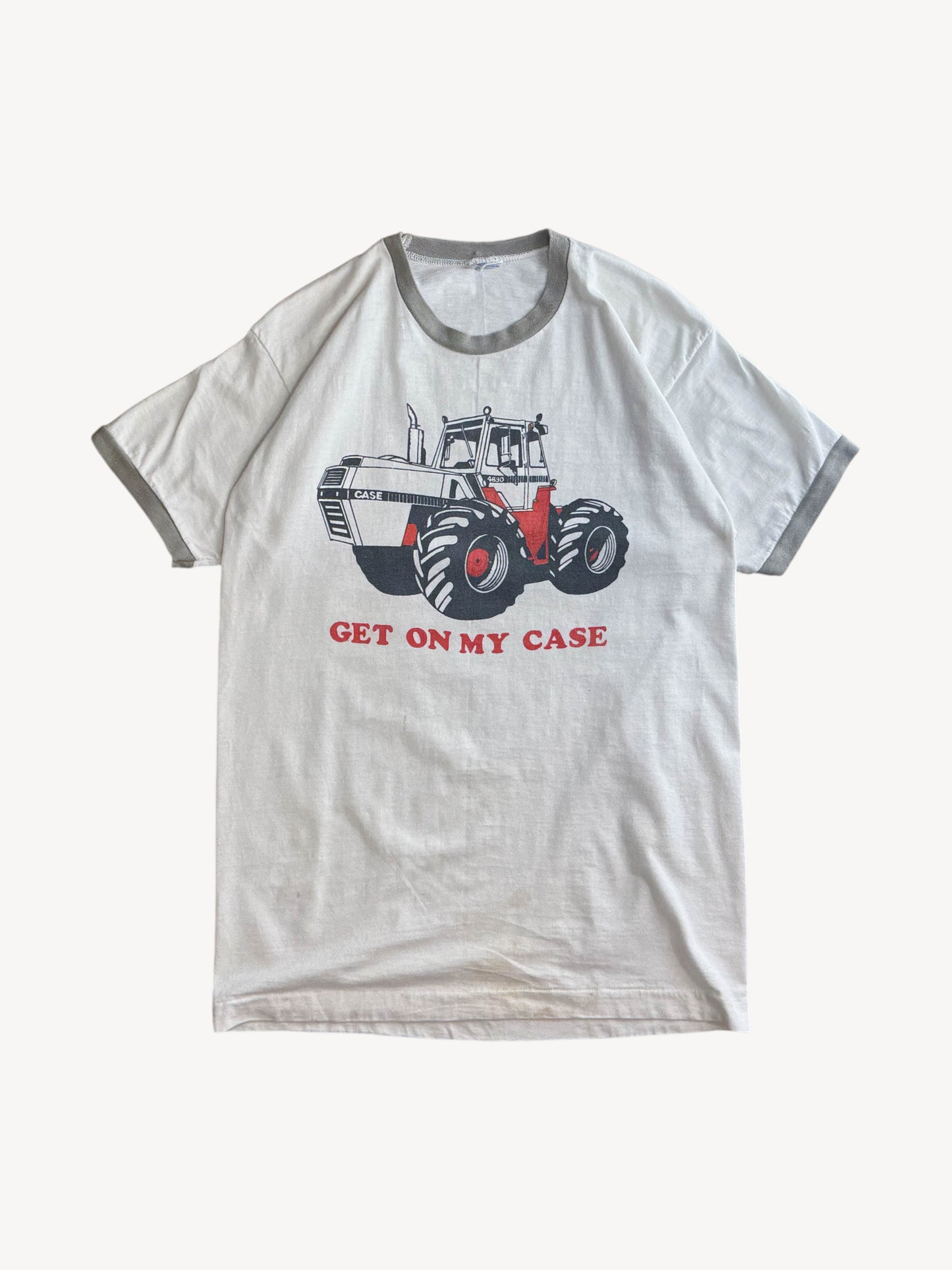 White t-shirt with a graphic of a tractor and text 'GET ON MY CASE' on a white background