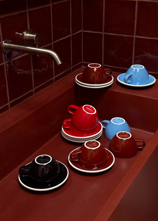 Set of colorful ceramic cups and saucers on a wooden surface with tiled wall background.