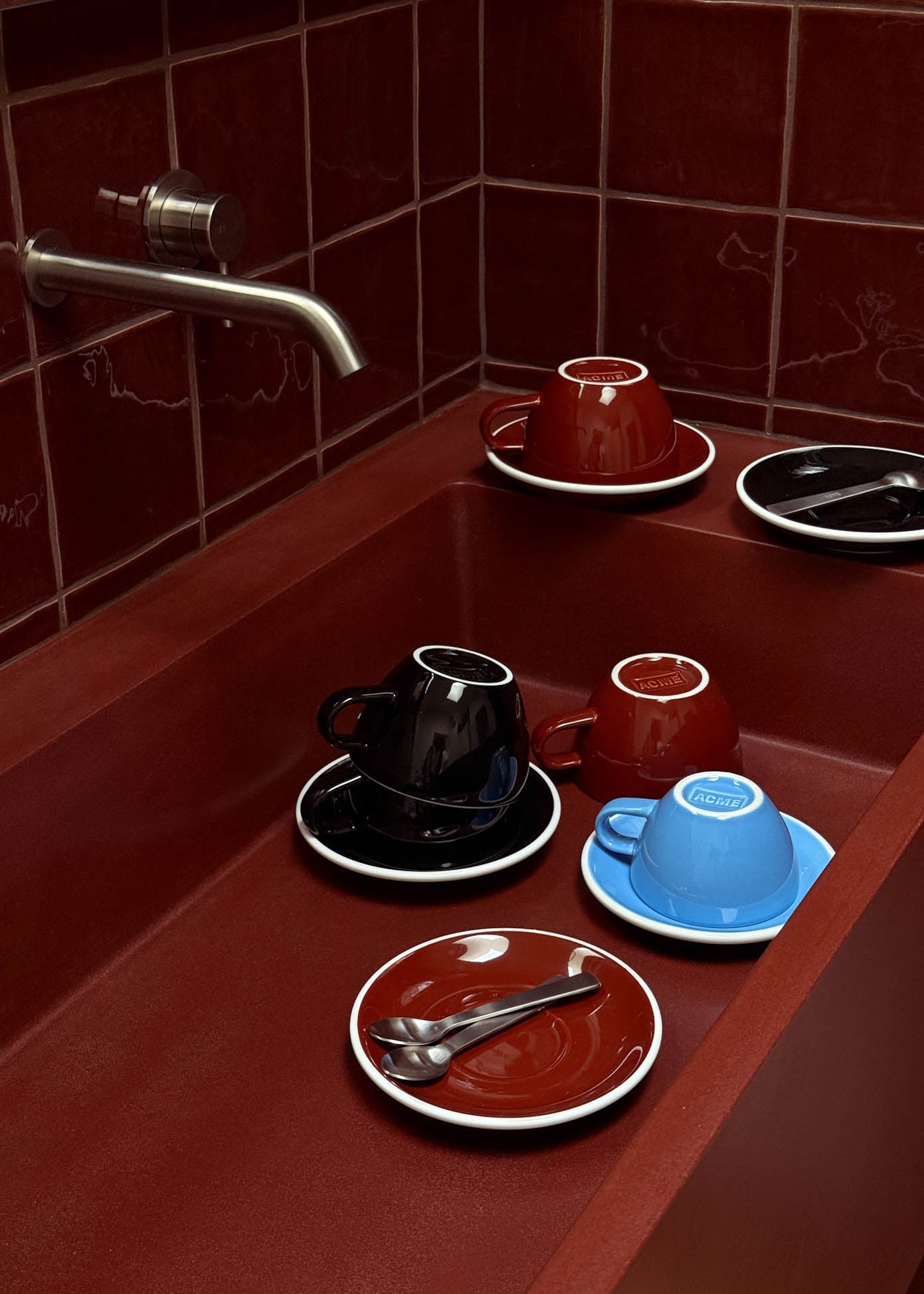 Cups and saucers on a red tiled countertop with a faucet.
