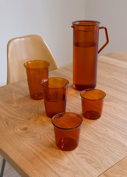 Set of brown glass tumblers and a pitcher on a wooden table.