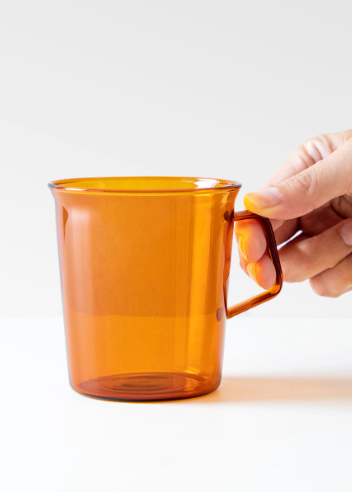Hand holding an amber glass mug against a white background