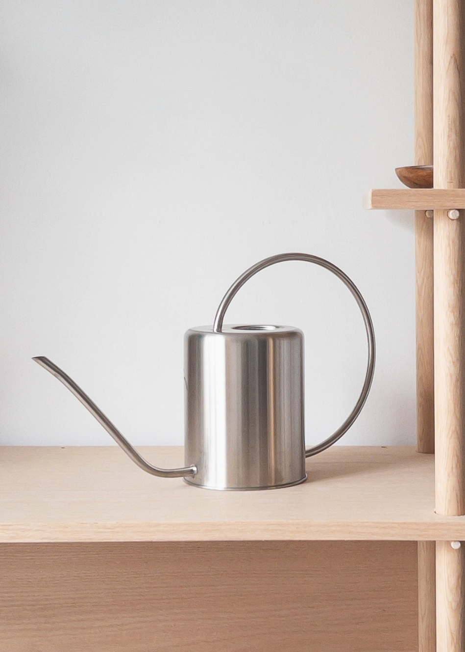 Silver stainless steele watering can on a wooden shelf