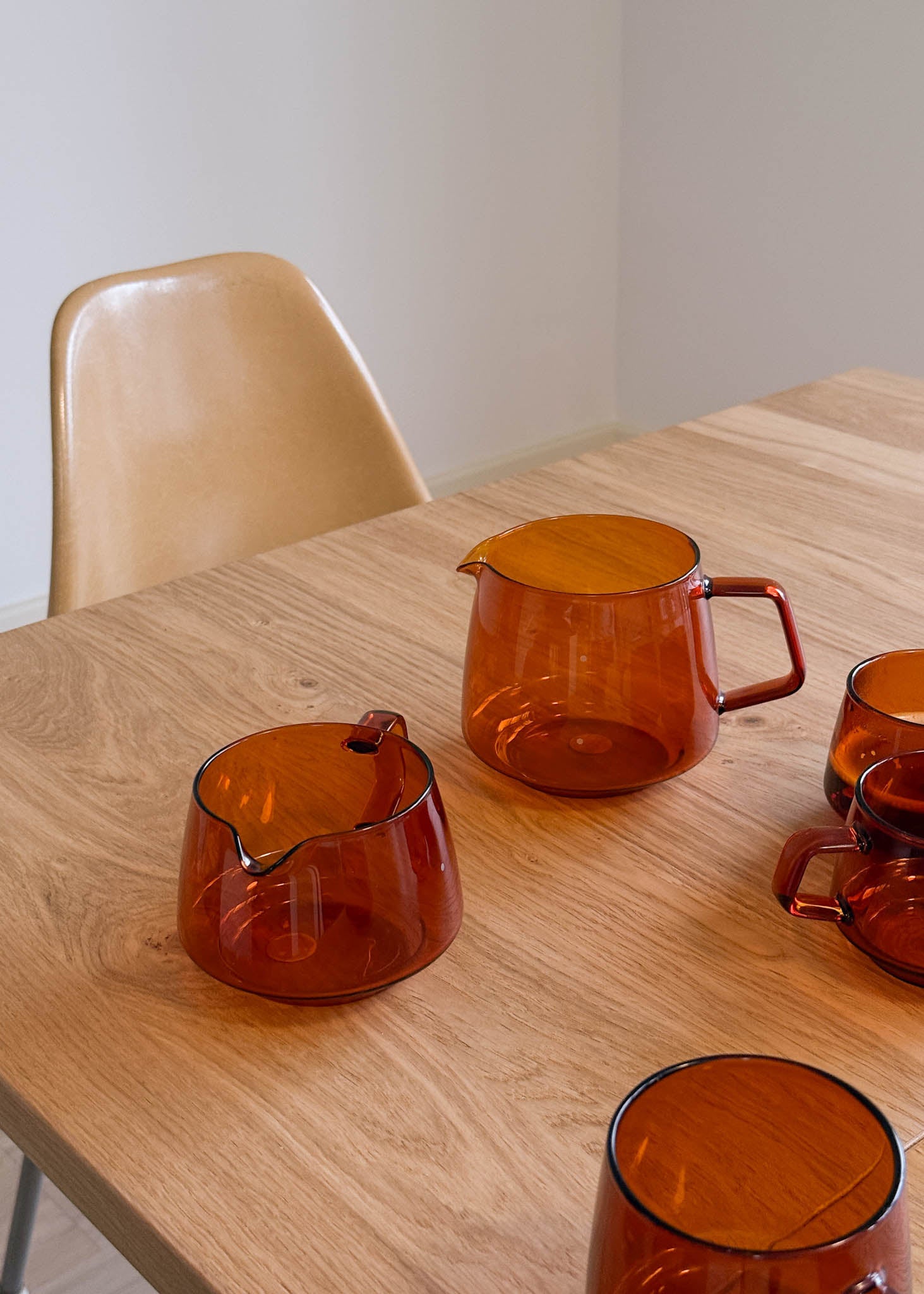 Set of amber glass pitchers on a wooden table with a beige chair.