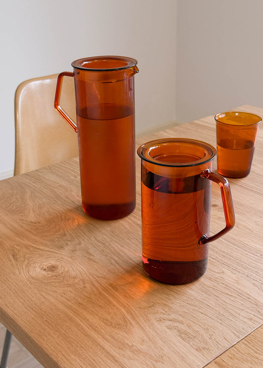 Set of orange glass pitchers and cups on a wooden table.