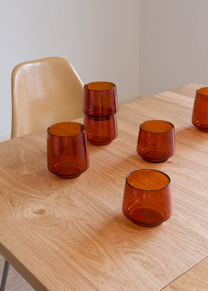 Set of amber glass tumblers on a wooden table with a neutral background