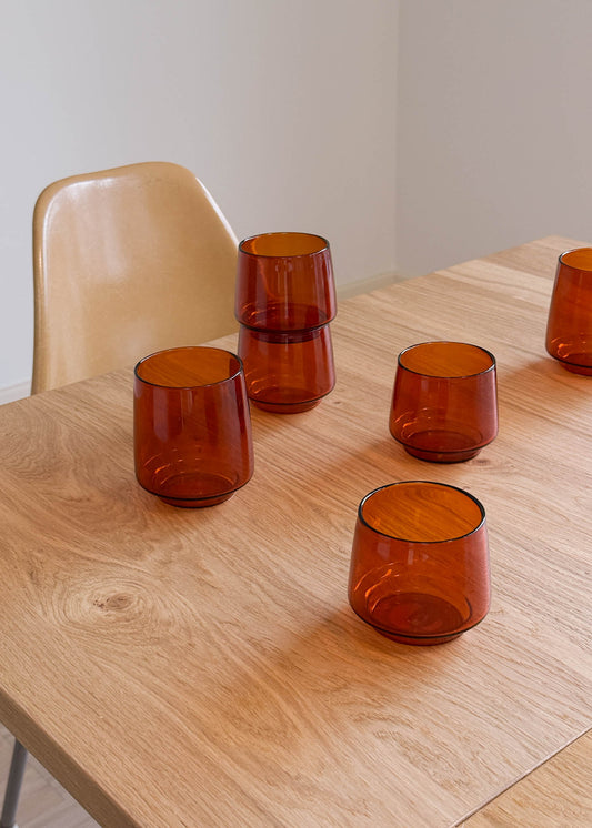 Set of amber glass tumblers on a wooden table with a neutral background