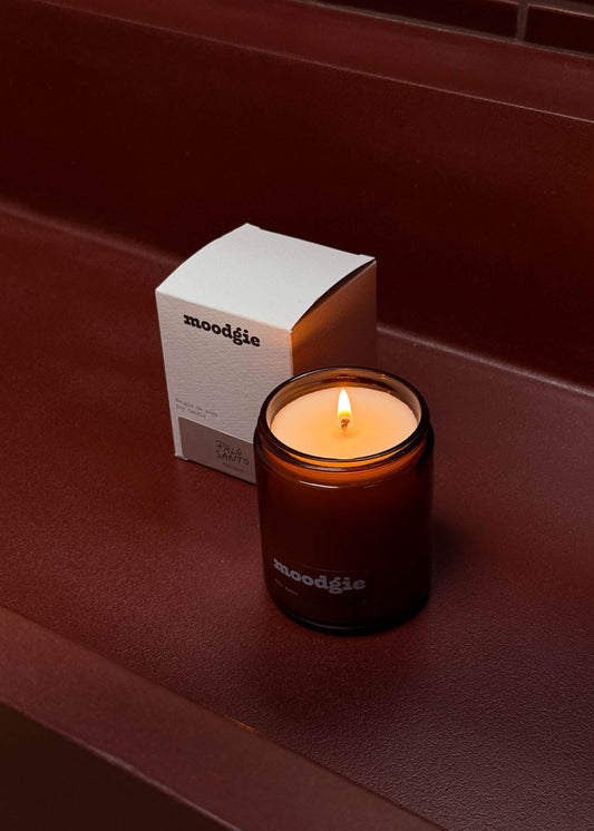 Moodgie candle with a lit flame on a dark surface next to its packaging box.
