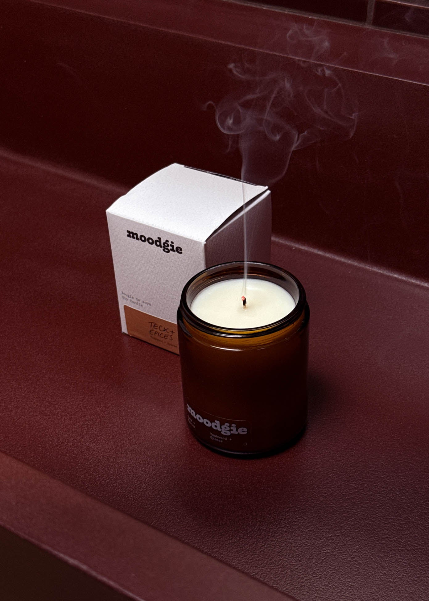 Moodie candle with smoke emitting from it on a red surface
