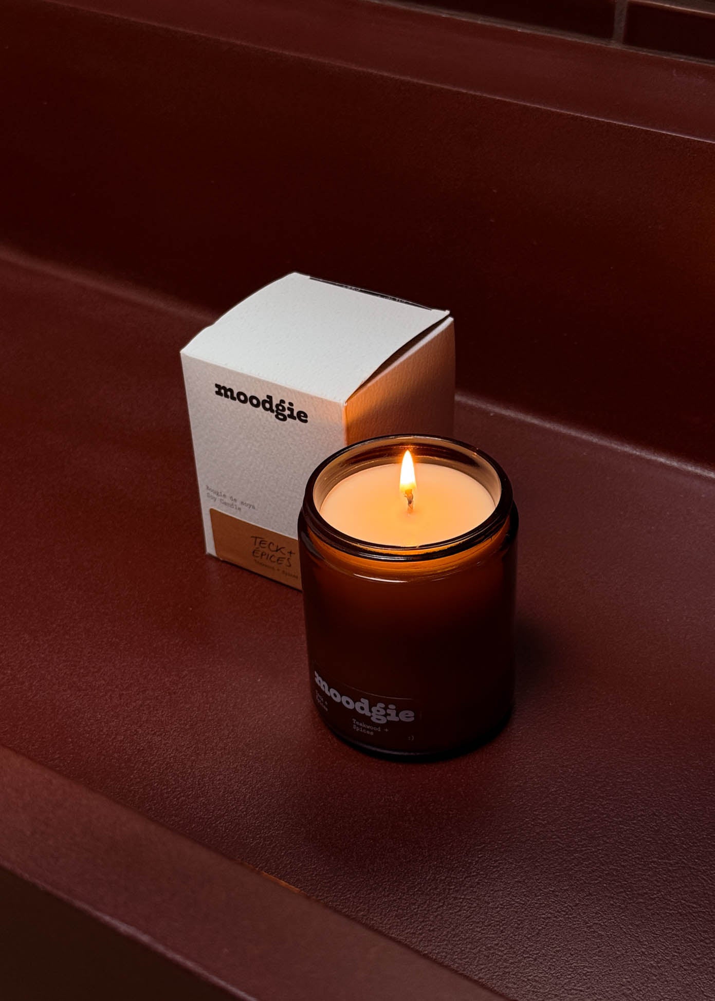 Moodgie candle and packaging on a dark red surface