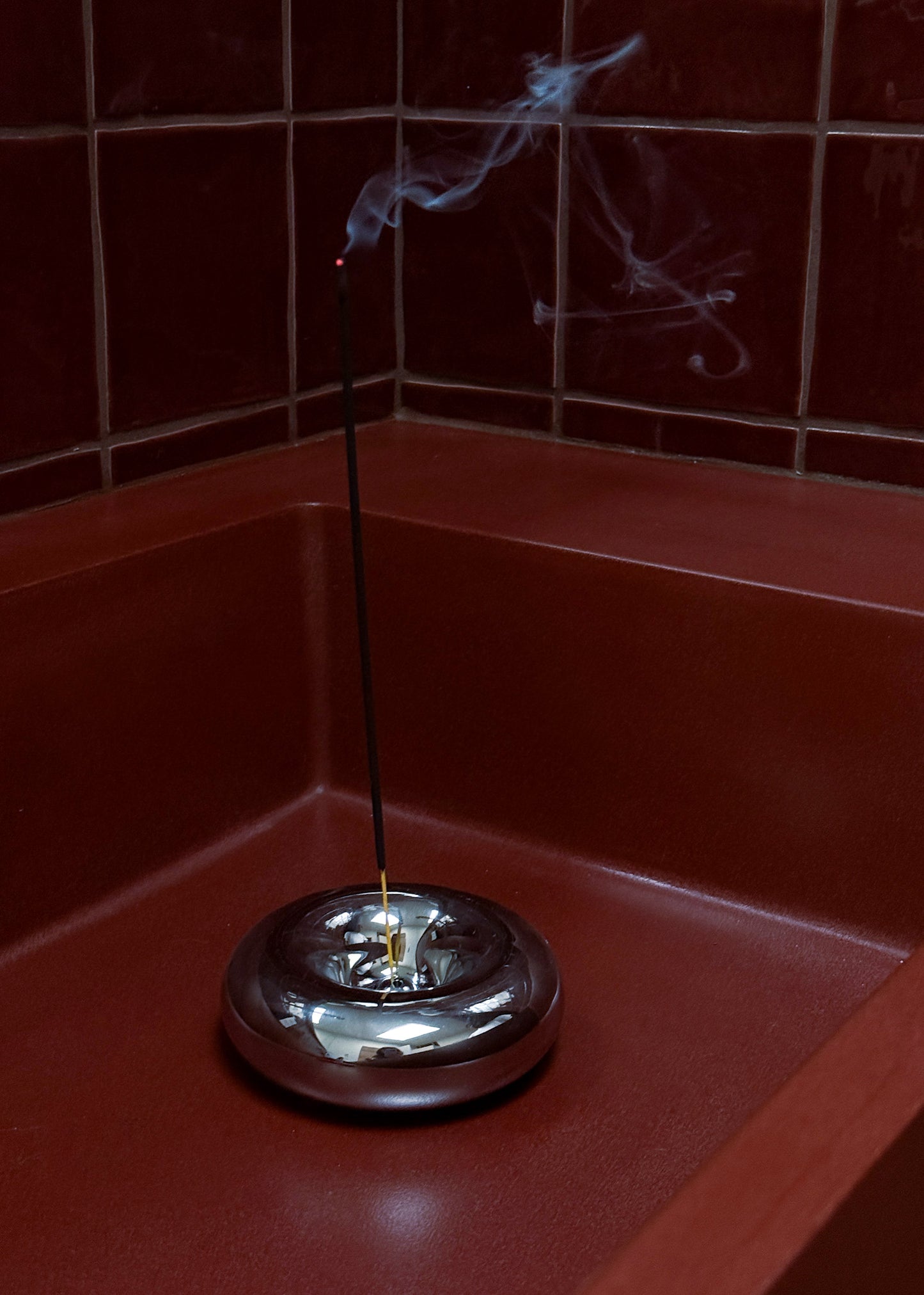 Donut shaped chrome ncense burner with smoke on a red tiled wall