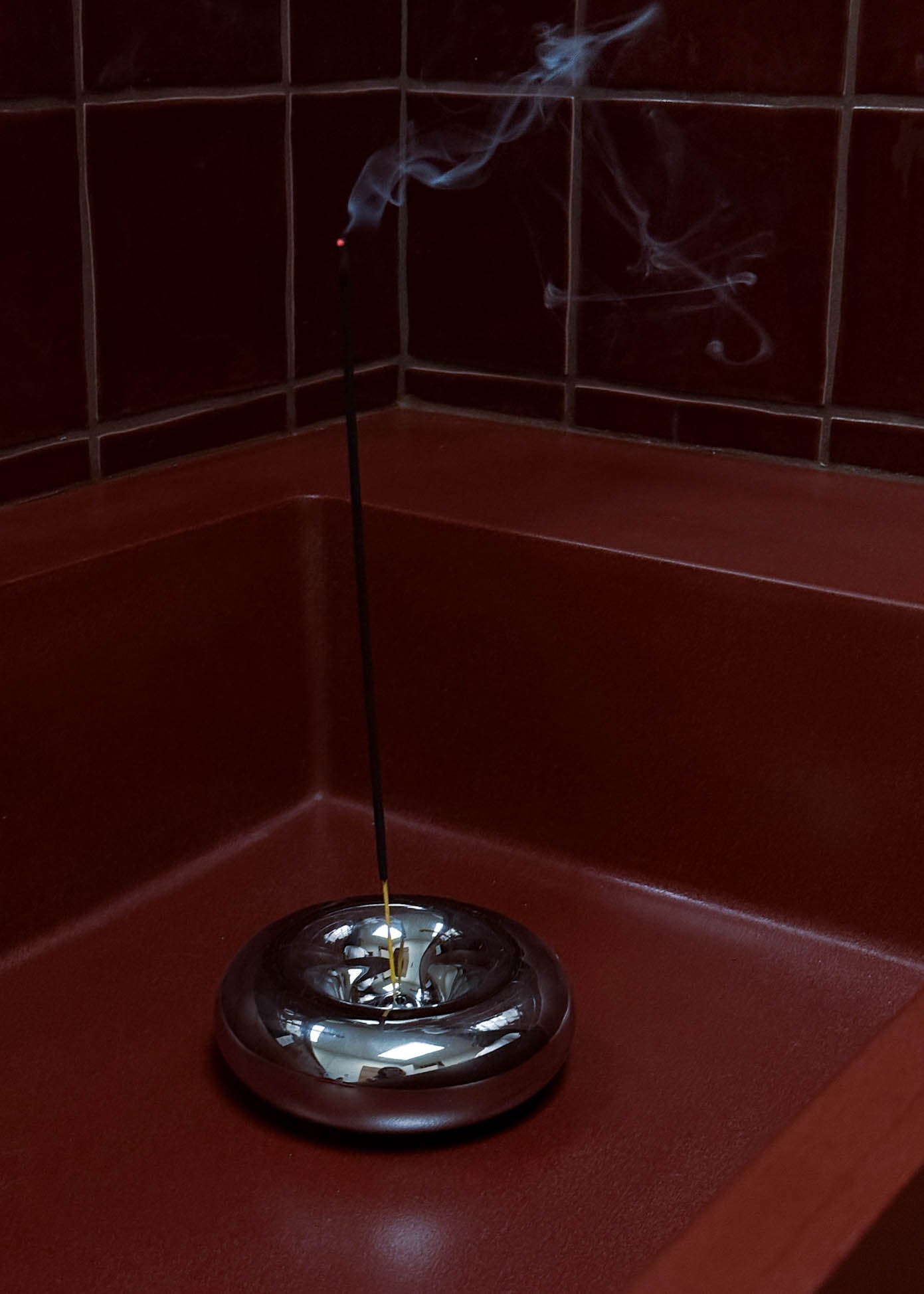 Incense stick with smoke on a red surface against a tiled wall
