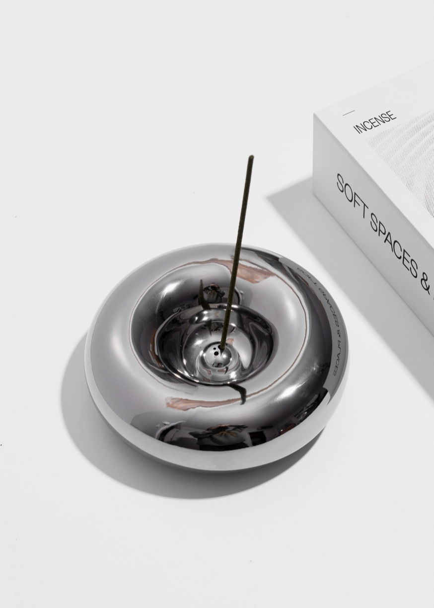 Chrome donut shaped incense burner with a single incense stick on a white background
