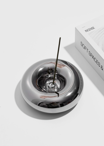 Chrome donut shaped incense burner with a single incense stick on a white background