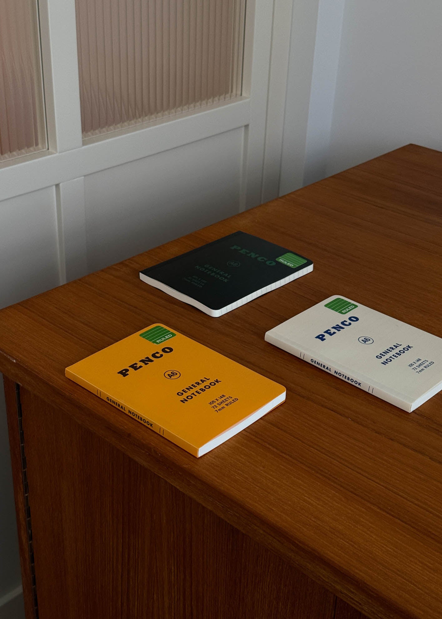 Three A6 size notebooks with 'PENCO' branding on a wooden surface.