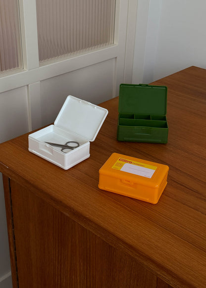 Three small plastic storage boxes in white, green and yellow on a wooden surface with a neutral background