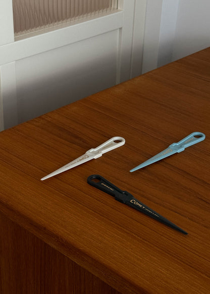 Three plastic letter openers on a wooden surface with a neutral background