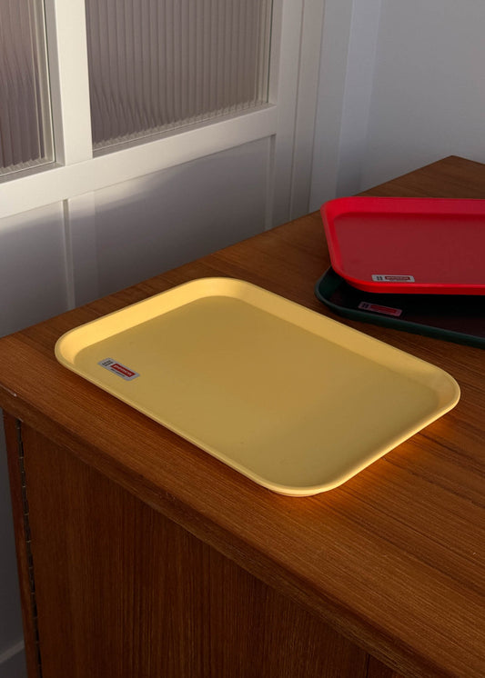 Yellow tray on a wooden surface with red and green trays in the background.