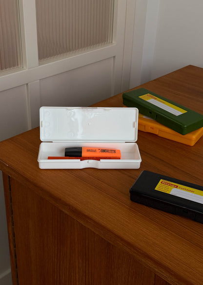 Orange marker in a white case on a wooden surface with a green box and black object.