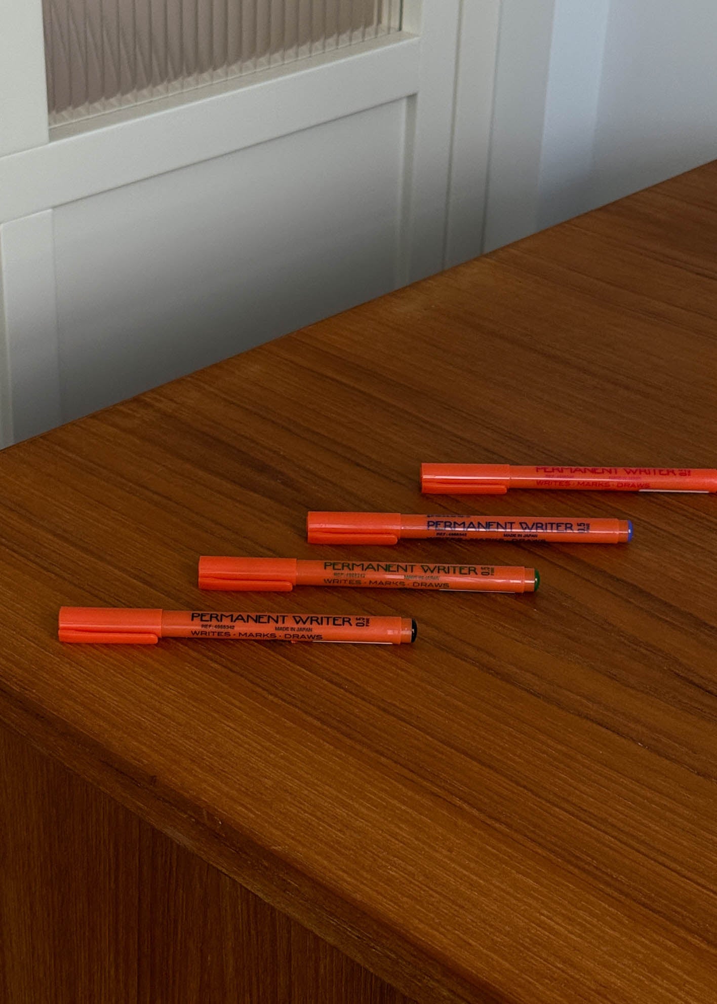 Orange markers on a wooden surface with a white cabinet in the background