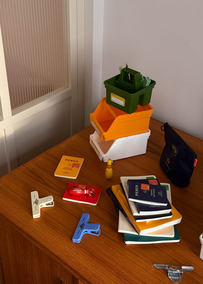 Stack of books, stationery items, and storage bins on a wooden surface.