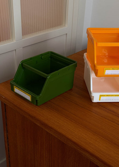 Green storage bin on a wooden surface with orange and white bins in the background.
