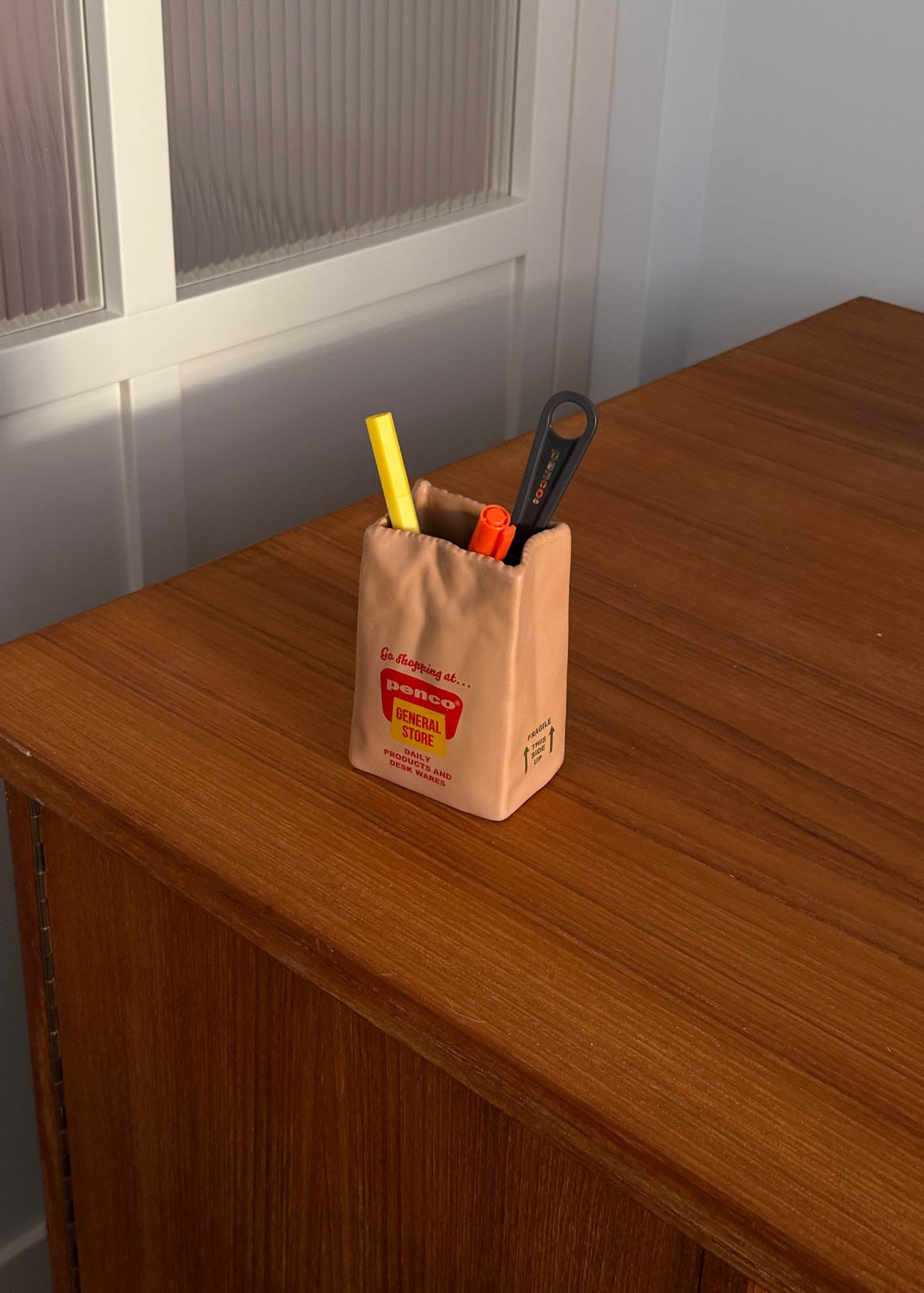 Pencil holder shaped like a brown paper bag with stationery items on a wooden surface
