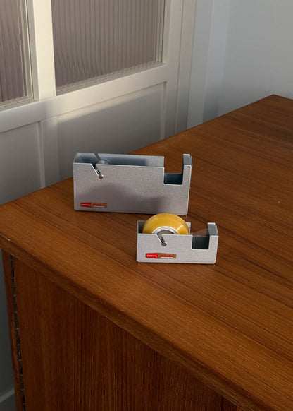 Two silver tape dispensers with tape on a wooden surface.