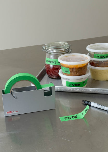 Containers with labels on a metal surface next to a green label applicator.