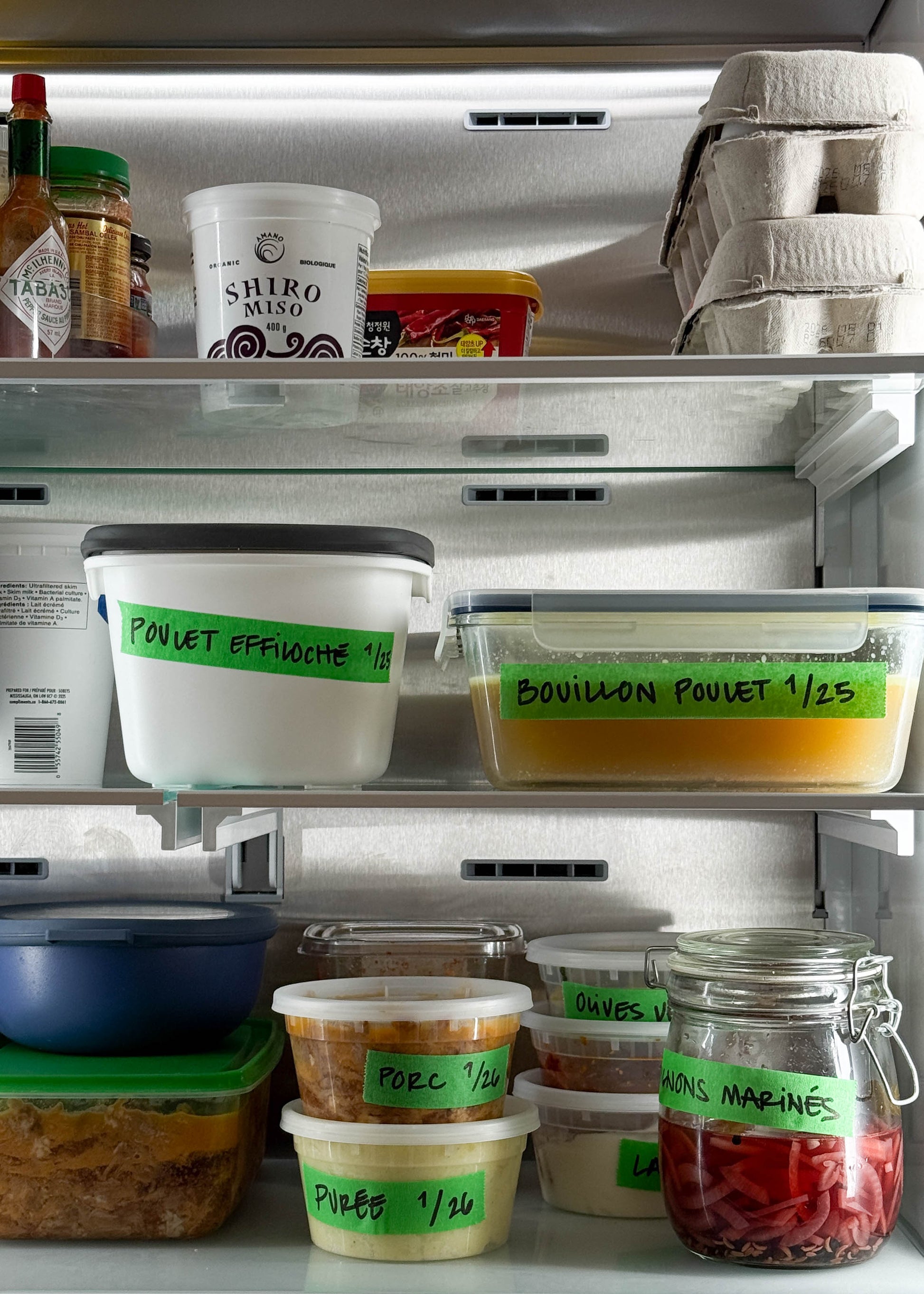 Refrigerator shelves with labeled food containers and a jar of pickles.