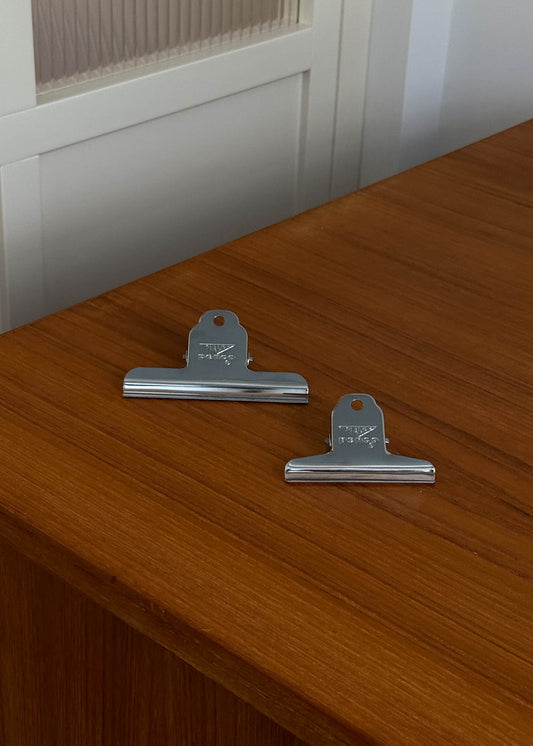 Two metal clips on a wooden surface with a white cabinet in the background.