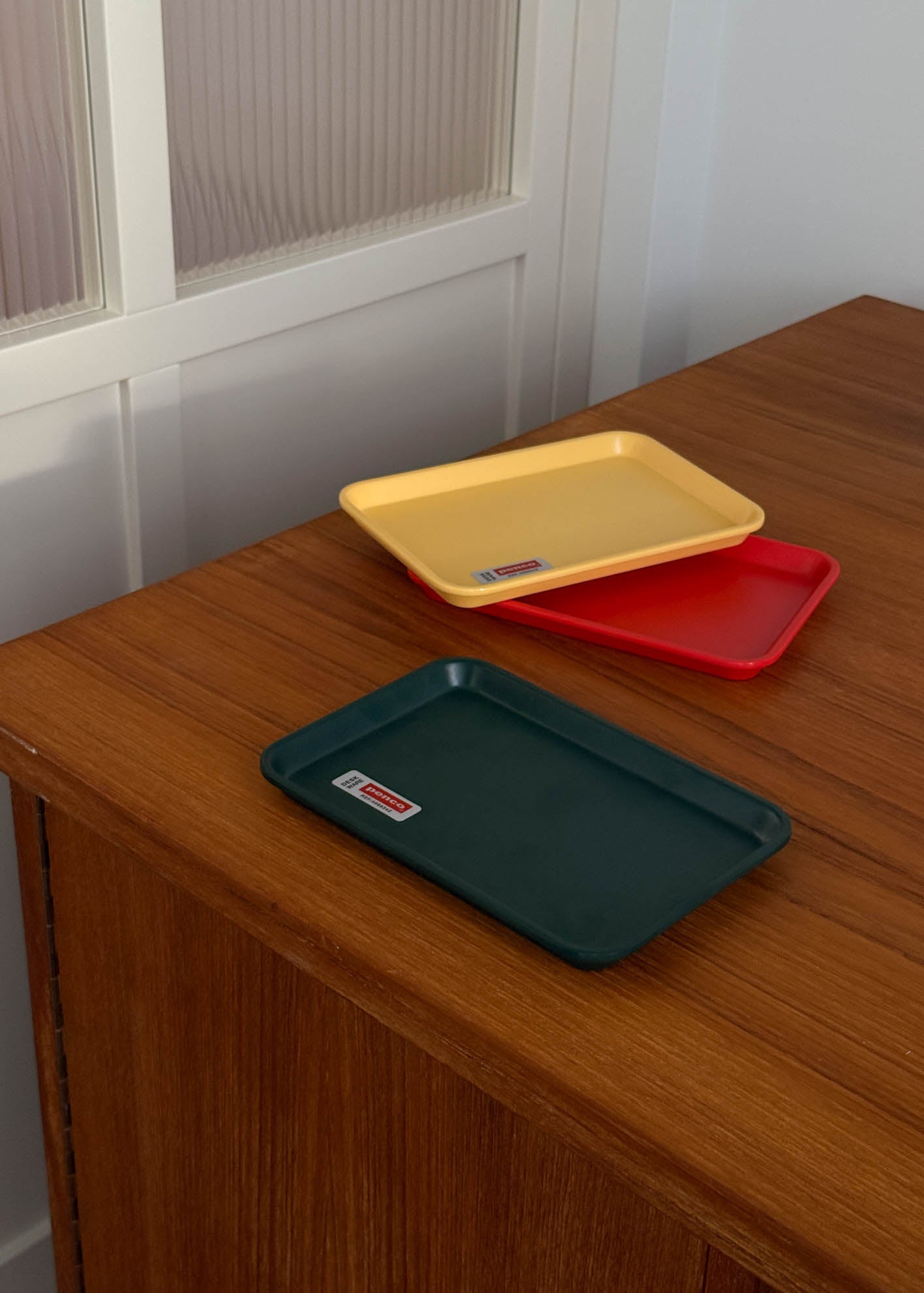 Three trays in yellow, red, and green on a wooden surface with a white wall background.