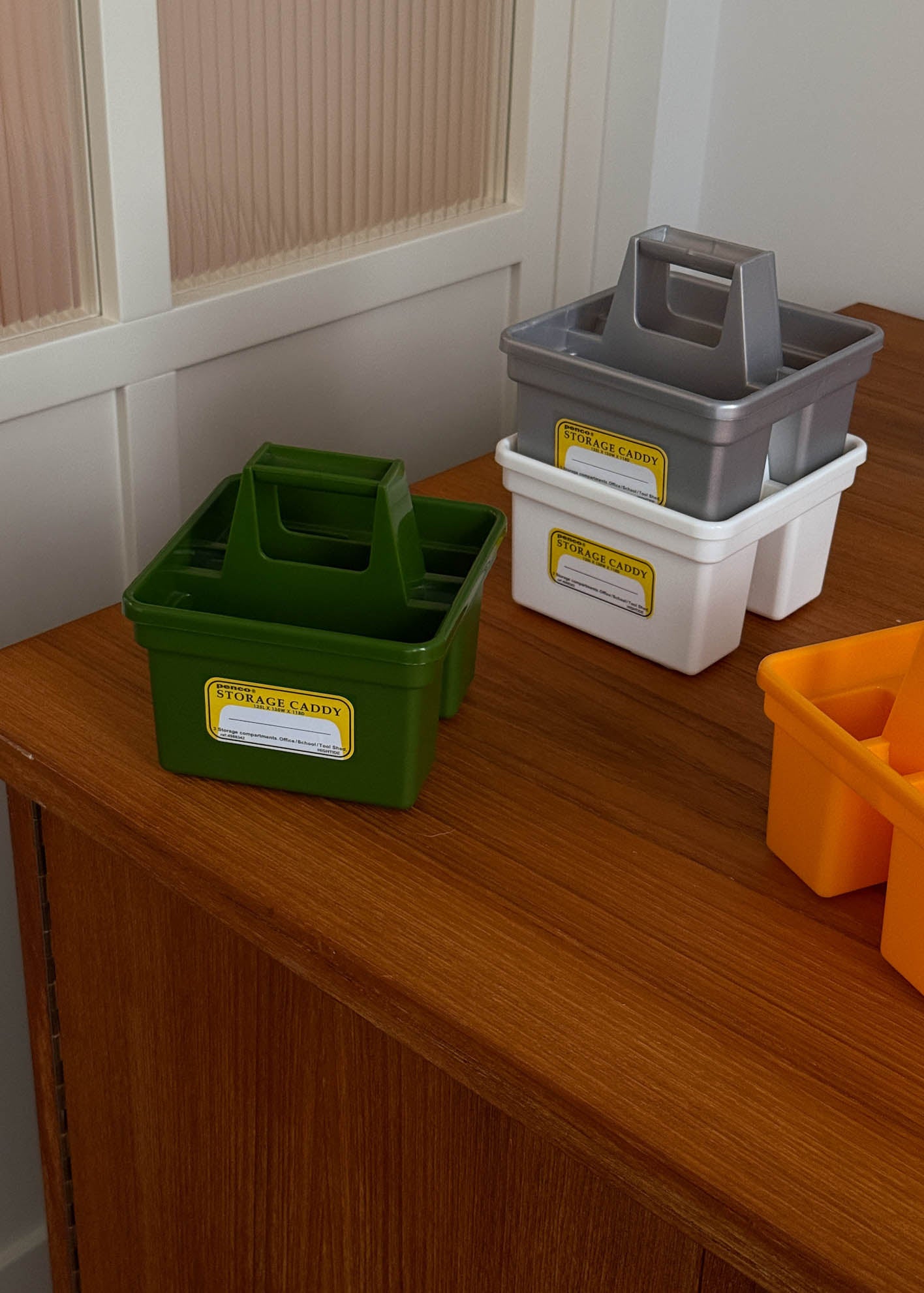 Four storage crates in green, gray, white, and yellow on a wooden surface.