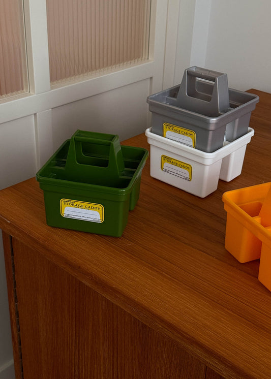 Four storage crates in green, gray, white, and yellow on a wooden surface.