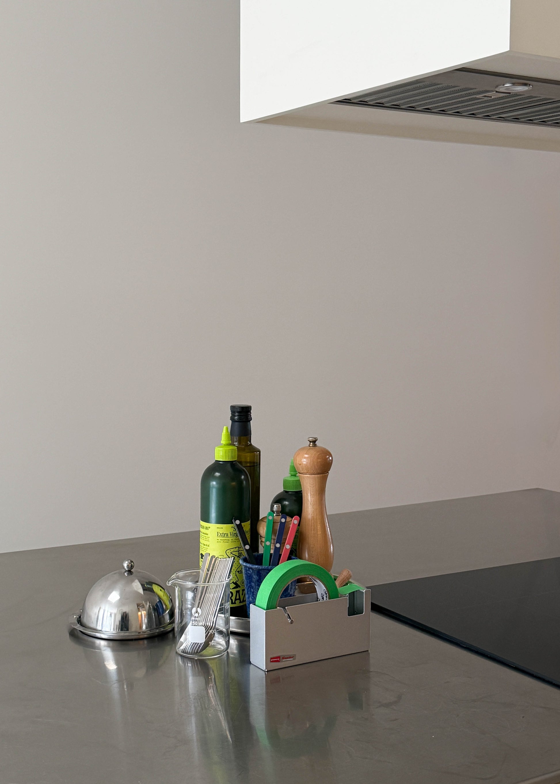 Kitchen counter with various items including bottles and a pepper grinder against a plain wall.